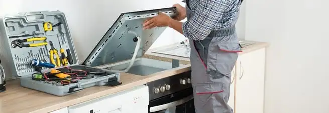 Cooktop repair technician lifting a built-in stovetop for service in Savannah, GA