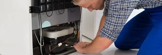 Refrigerator repair technician servicing the compressor and condenser area in Savannah, GA