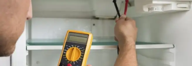 Refrigerator repair technician testing electrical components with a multimeter in Savannah, GA